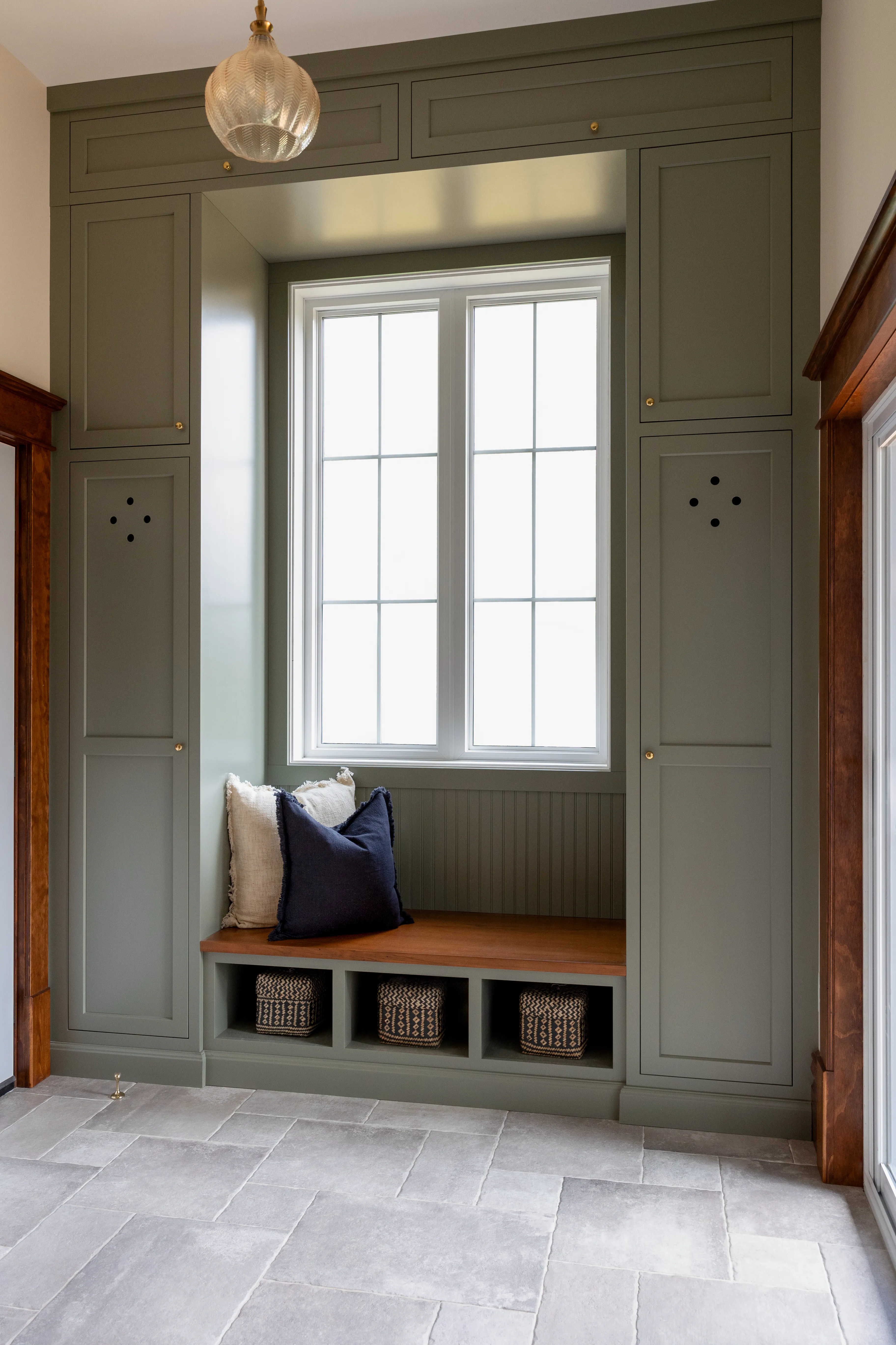 Custom sage green mudroom with built-in bench and cubbies by Heirlooms